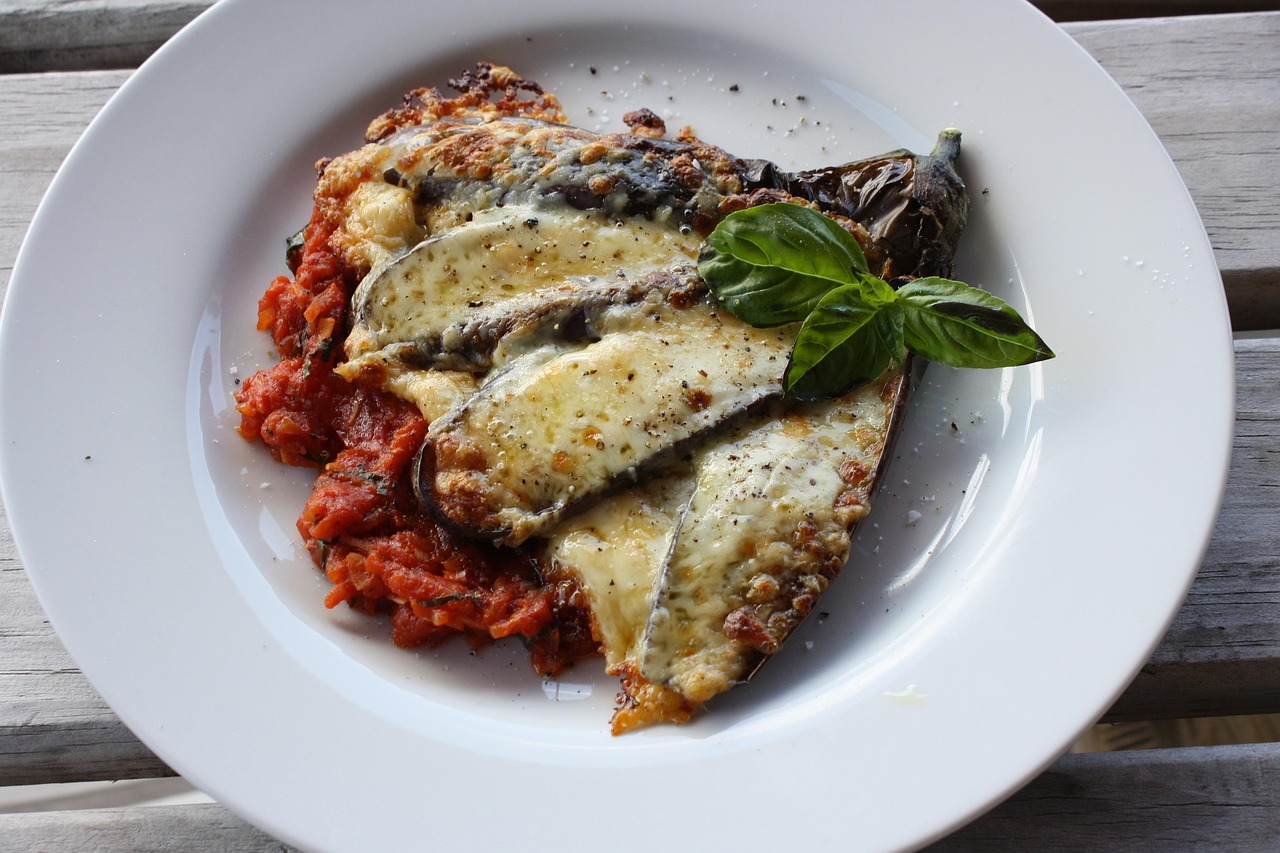 Porzione di parmigiana leggera con melanzane, pomodoro e mozzarella filante su piatto bianco.