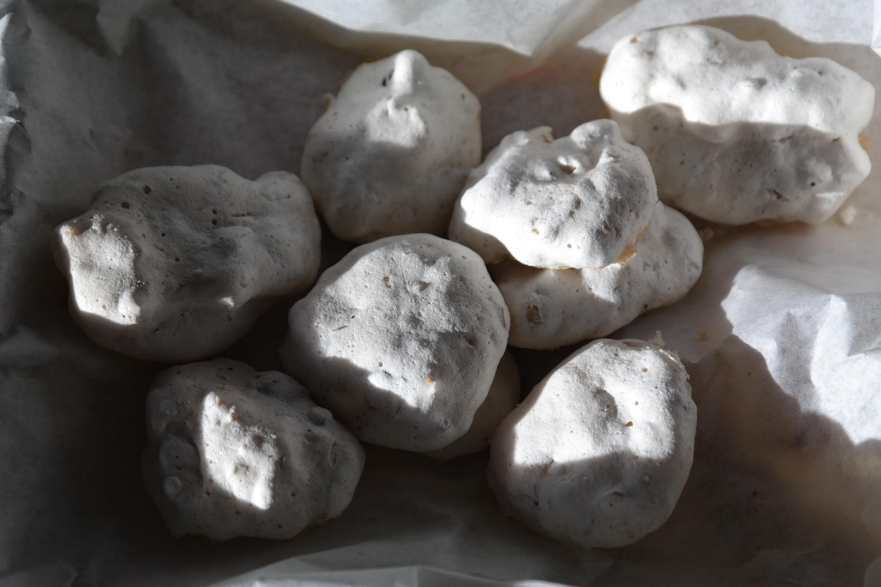 Meringhe bianche perfette su una teglia, pronte per la cottura a forno bassissimo e sportello socchiuso.